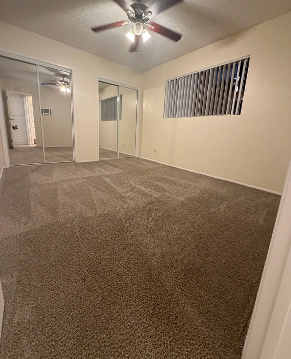A room with a ceiling fan and carpeted floor.